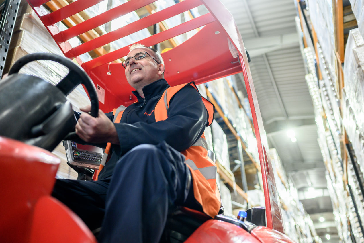 A close-up of a happy employee of Knowles riding a forklift